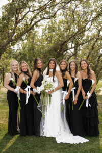 Bridesmaid in black with single lily bouquets tied with ribbons.