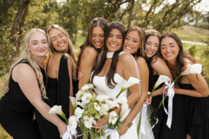 bridesmaids and bride squeezed together holding flowers and smiling.