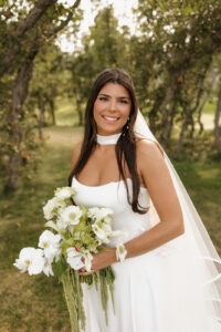 Bride in her wedding dress and veil and neck scarf. Holding her green and white floral bouquet.