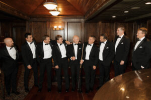 Groomsmen in black tuxes smiling with a cue in a speakseasy.