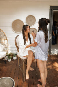 Bride laughing with her bridesmaid while she puts her lipgloss on in their pjs and robes.